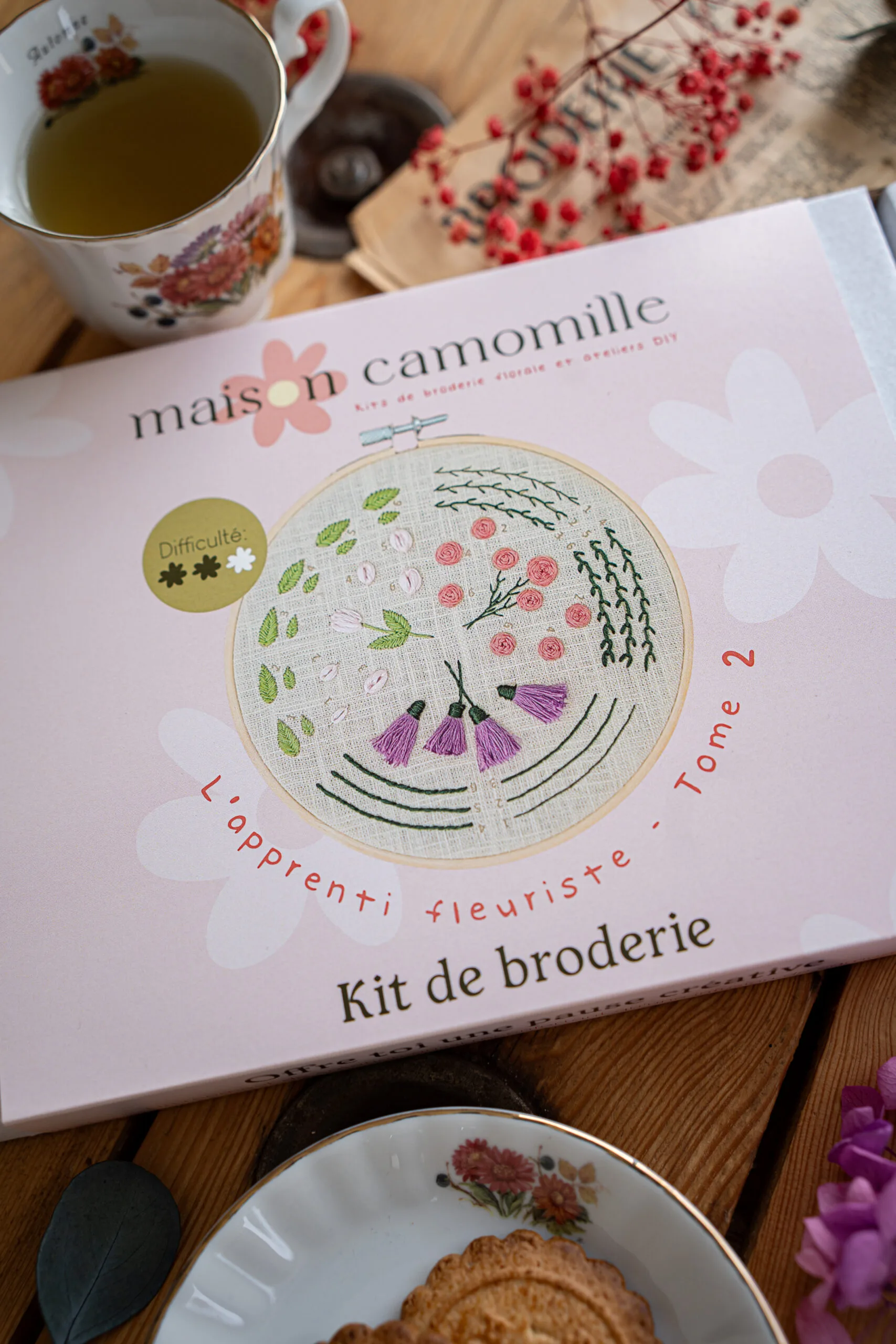 Kit broderie "L'apprenti fleuriste" Tome 2 dans son emballage, prêt à être déballé, posé sur une table avec une petite tasse de thé