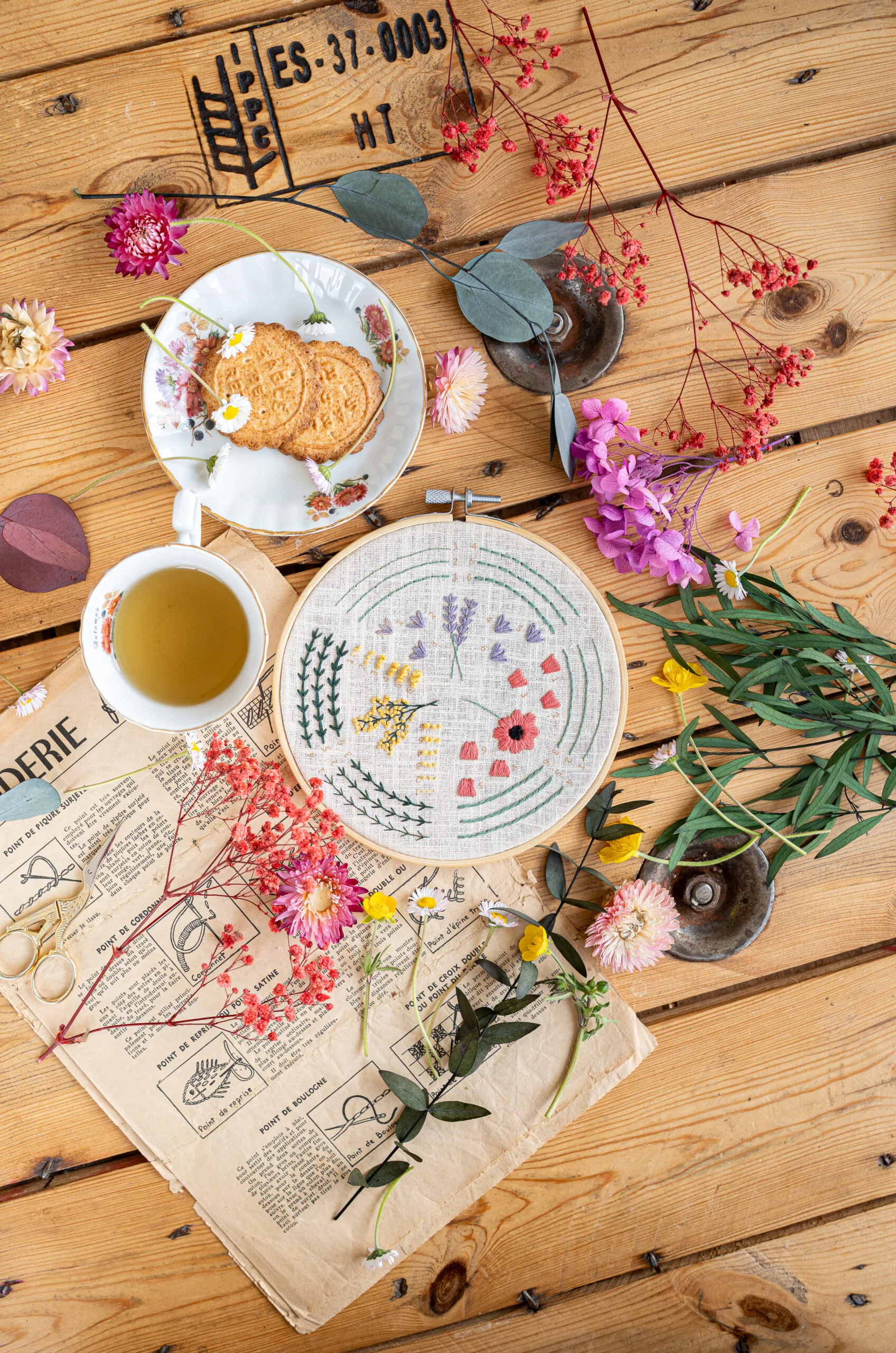 Modèle fini du Kit broderie "L'apprenti fleuriste" Tome 1 entouré de sa tasse de thé et de petits gateaux pour une pause créative
