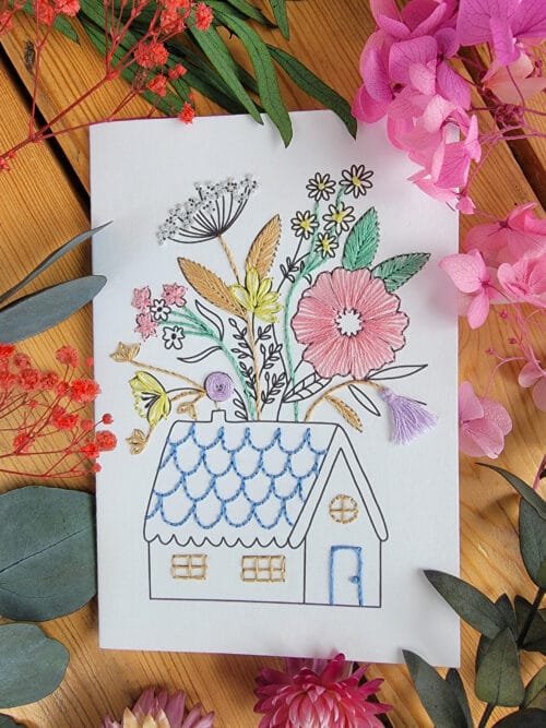 Carte à broder représentant une maison de campagne dont le toit se fleurit
