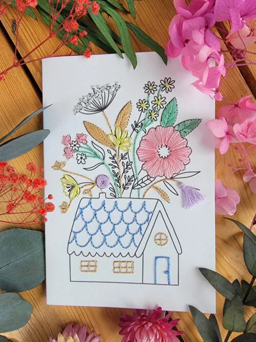 Carte à broder représentant une maison de campagne dont le toit se fleurit