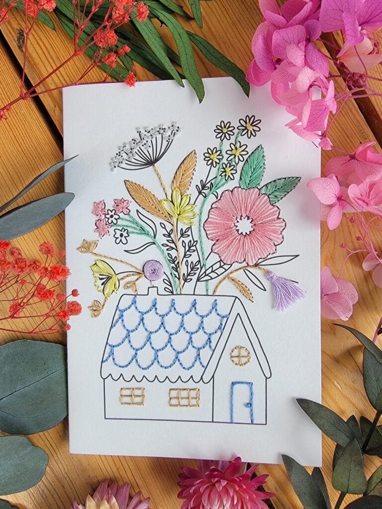 Carte à broder représentant une maison de campagne dont le toit se fleurit