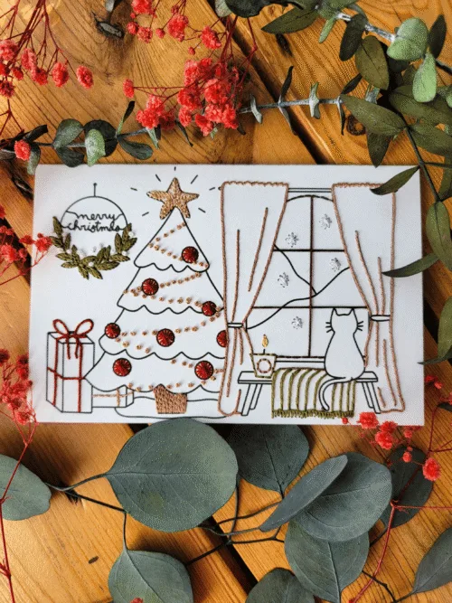 Carte à broder d'un Noel à a maison, sapin décoré, et chat regardant par la fenetre